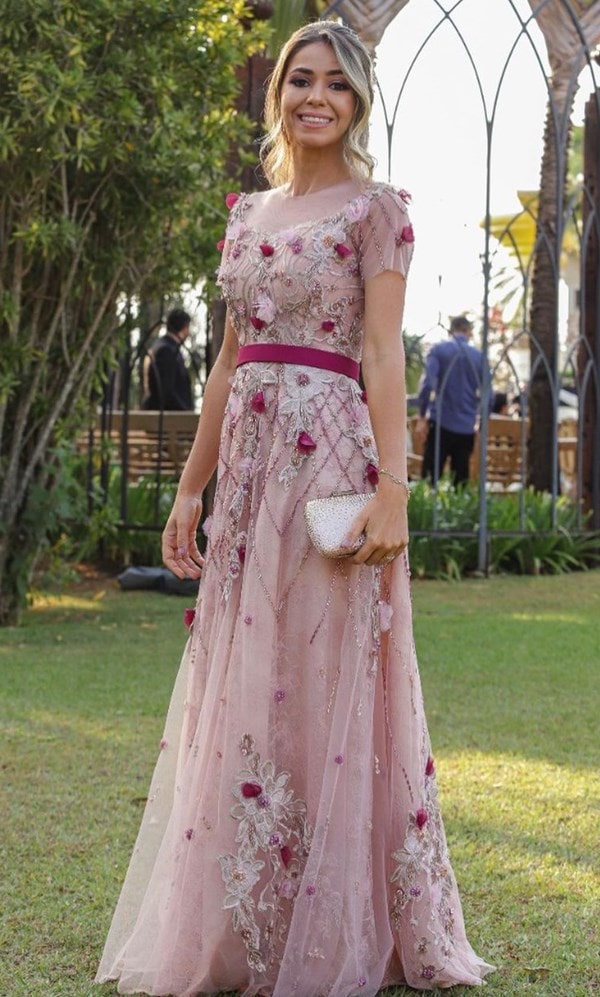 Madrinha de casamento ao ar livre usando vestido de festa longo nude rose de tule com cinto de tecido veludo e bordado de flores 3D em tons de fúcsia